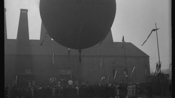 Dans quelle ville se situe cette préparation d'une ascension en ballon et quelle industrie représente ce bâtiment ?